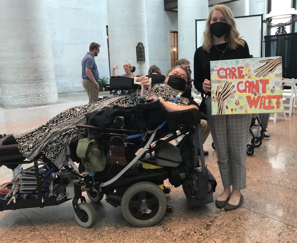 Maria Matzik and Alexia Kemerling in the atrium. Alexia is holding a sign that says, "Care Can't Wait."